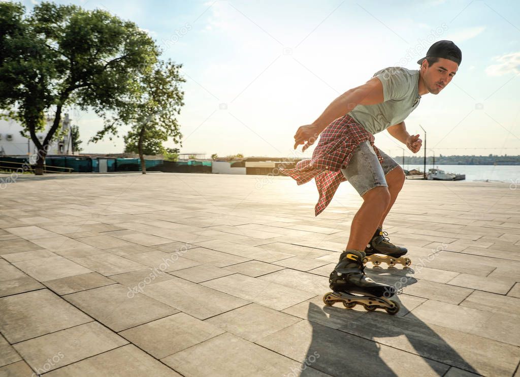 Handsome young man roller skating on pier near river, space for text