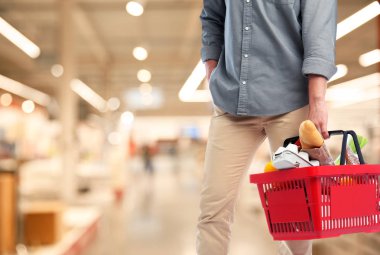 Alışveriş sepeti farklı ürünlerle dolu bir süpermarkette, yakın çekimde genç bir adam. Metin için alan 