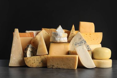 Different types of delicious cheese on table against black background clipart