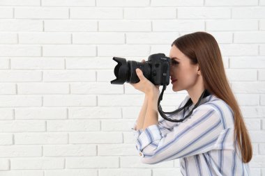 Profesyonel fotoğrafçı beyaz tuğla duvar yakınında fotoğraf çekmek