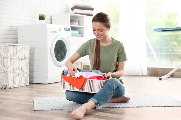 Junge Frau mit Korb sauberer Wäsche auf dem Fußboden im Zimmer — Stockfoto