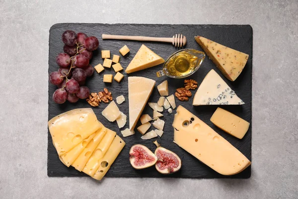 Placa de ardósia com diferentes tipos de deliciosos queijos e lanches na mesa cinza, vista superior — Fotografia de Stock