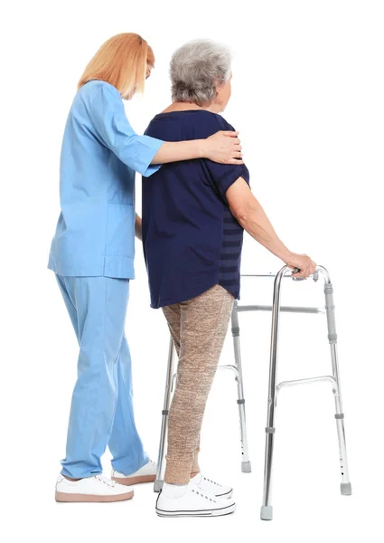 Cuidador ayudando a anciana con marco de caminar sobre fondo blanco — Foto de Stock