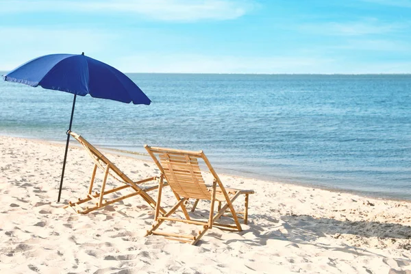 Esvaziar espreguiçadeiras de madeira e guarda-chuva na costa arenosa. Acessórios de praia — Fotografia de Stock