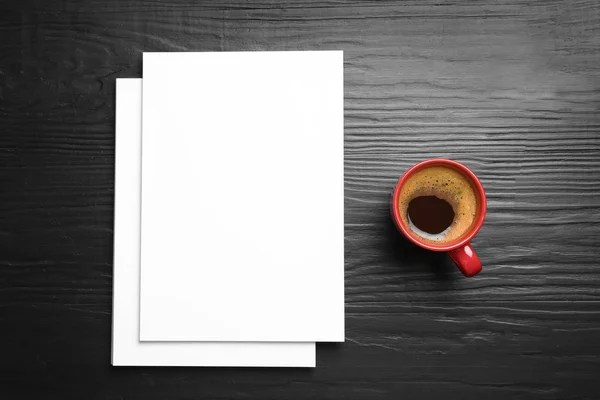 Leere Papierbögen für Broschüren und Kaffeebecher auf schwarzem Holzgrund, flach gelegt. Attrappe — Stockfoto