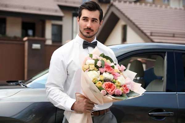 Joven hombre guapo con hermoso ramo de flores cerca de coche al aire libre —  Fotos de Stock