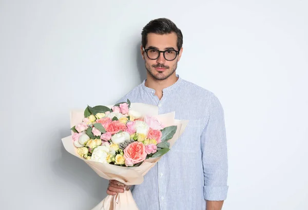 Joven hombre guapo con hermoso ramo de flores sobre fondo claro —  Fotos de Stock