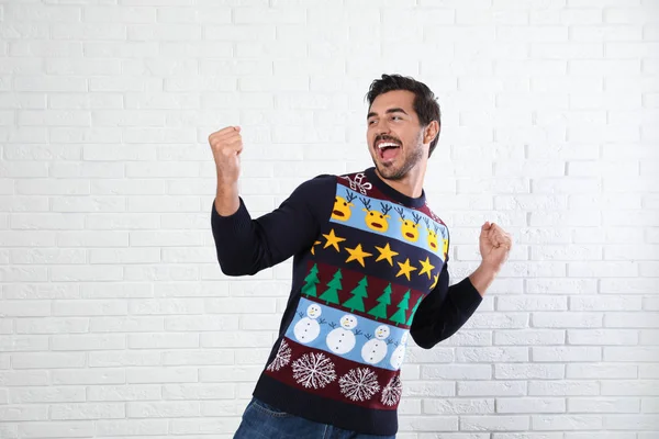 Emotional young man in Christmas sweater near white brick wall — Stock Photo, Image