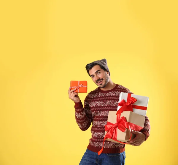 Hombre feliz en jersey de Navidad y sombrero sosteniendo cajas de regalo sobre fondo amarillo —  Fotos de Stock