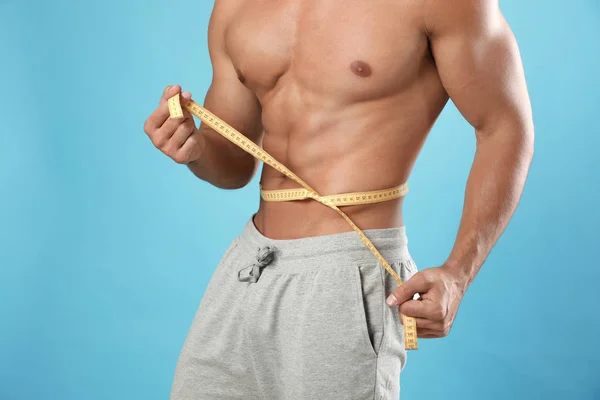 Young man with slim body using measuring tape on light blue background, closeup view — Stock Photo, Image