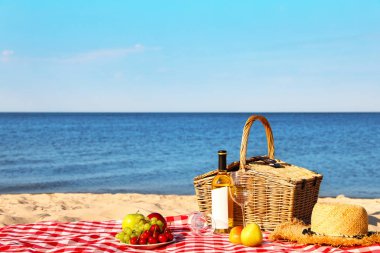 Güneşli plajda piknik sepeti ve ürünleri ile damalı battaniye. Metin alanı