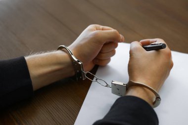 Kelepçeli suçlu masada itiraf yazıyor, yakın çekim