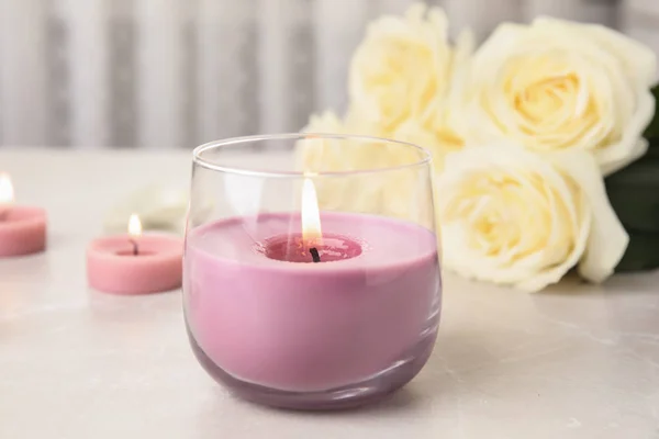 Burning candle in glass holder and roses on light table — Stock Photo, Image