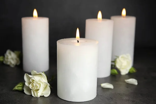 Burning candles and flowers on dark grey table