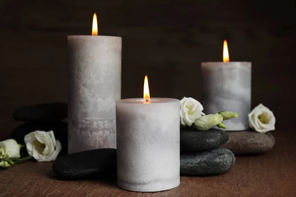 Velas ardientes, piedras de spa y flores sobre mesa de madera —  Fotos de Stock