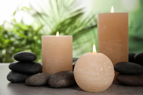 Горящие свечи и спа-камни на столе на размытом зеленом фоне — стоковое фото