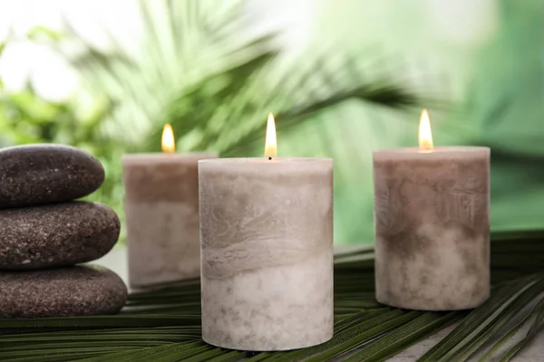 Hořící svíčky a lázeňské kameny s palmovým listem na stole proti rozmazané zelené pozadí — Stock fotografie