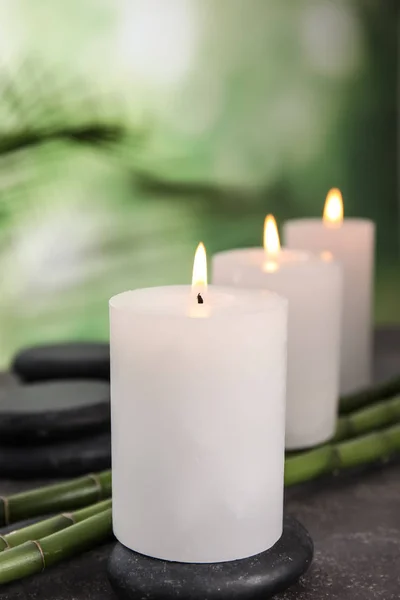 Горящие свечи, спа-камни и бамбуковые ростки на сером столе на размытом зеленом фоне — стоковое фото
