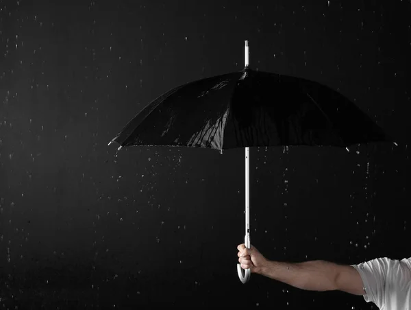 Karanlık arka plana karşı yağmur altında siyah şemsiye tutan adam, yakın çekim — Stok fotoğraf