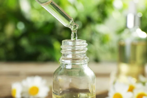 Dropping essential oil into bottle on blurred background, closeup — Stock Photo, Image