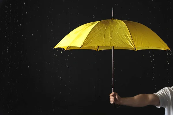 黒い背景に雨の下で黄色い傘を持つ男、クローズアップ — ストック写真