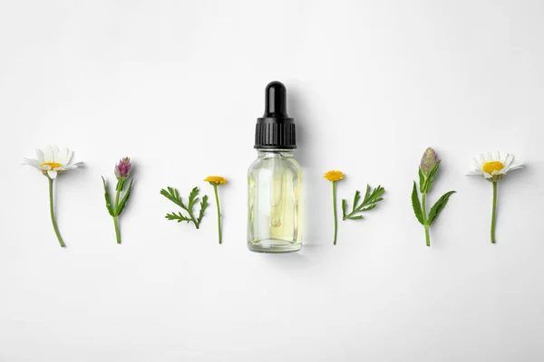 Fles etherische olie en wilde bloemen op witte achtergrond, bovenaanzicht — Stockfoto