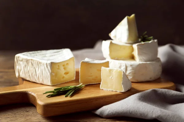 Placa de madeira com deliciosos queijos na mesa — Fotografia de Stock