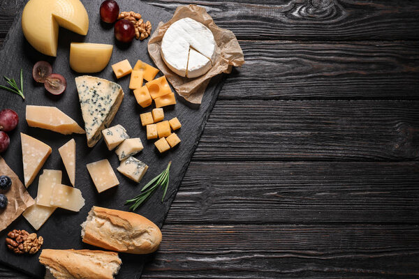 Different types of delicious cheese served on black wooden table, top view. Space for text