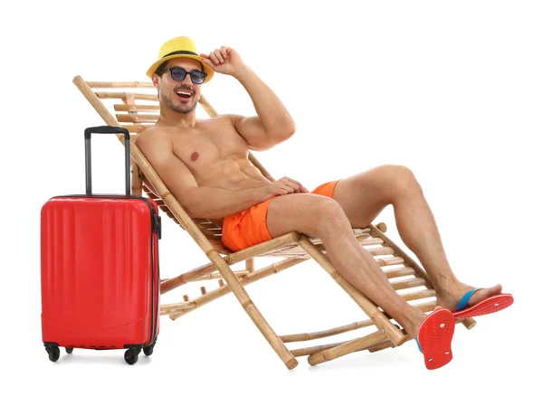 Junger Mann mit Koffer auf Sonnenliege vor weißem Hintergrund. Strandzubehör — Stockfoto