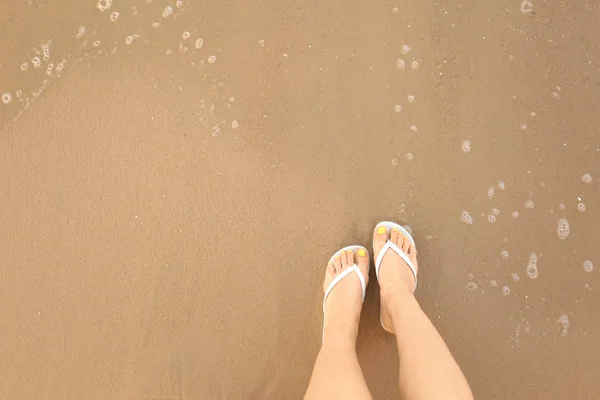 Bovenaanzicht van de vrouw met witte flip flops op zand in de buurt van zee, ruimte voor tekst. Strand accessoires — Stockfoto