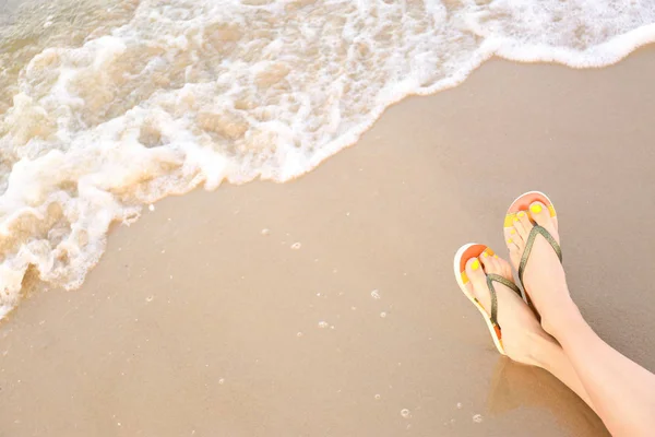 Närbild av kvinna med snygga flip flops på sand nära havet, utrymme för text. Strandtillbehör — Stockfoto