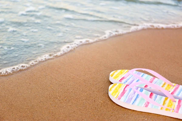 Des tongs élégantes sur le sable près de la mer, espace pour le texte. Accessoires de plage — Photo