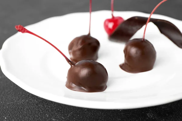 Plate of chocolate dipped cherries on black table, closeup — Stock Photo, Image