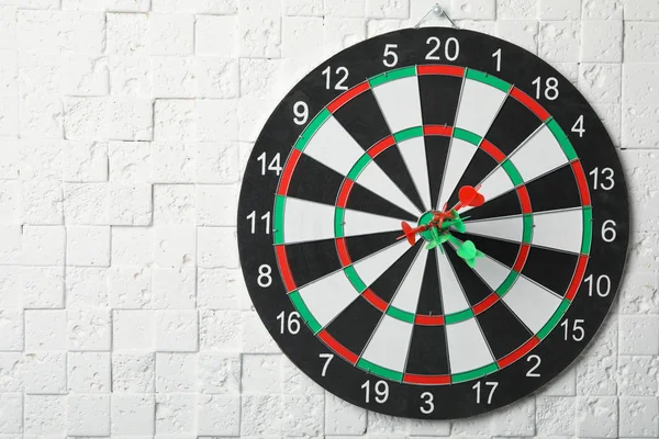 Dart board with arrows hitting target on white textured wall. Space for text