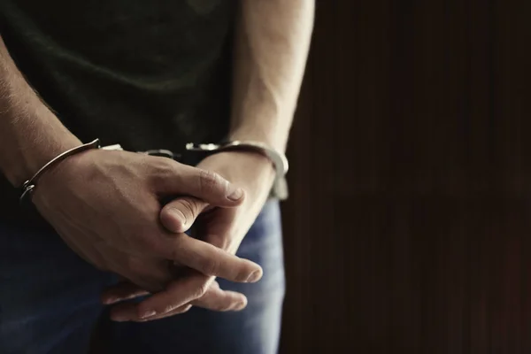 Человек, задержанный в наручниках на размытом деревянном фоне, место для текста. Уголовное право — стоковое фото