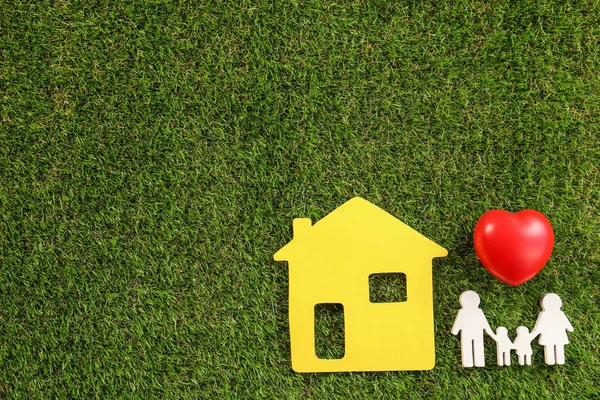 Figuras de la familia, el corazón rojo y la casa amarilla sobre hierba verde, la puesta plana. Espacio para texto — Foto de Stock