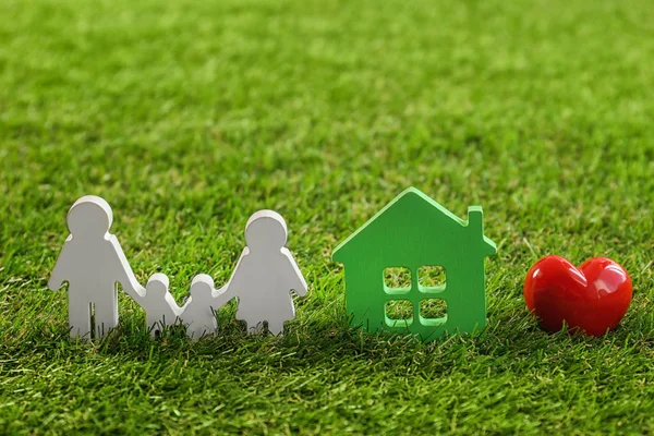 Figuras de familia, corazón rojo y casa sobre hierba verde — Foto de Stock