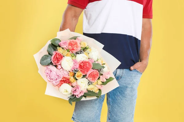 Jovem homem bonito com lindo buquê de flores no fundo amarelo, vista close-up — Fotografia de Stock