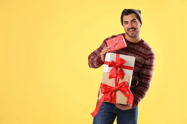 Счастливый человек в рождественском свитере и шляпе держит подарочные коробки на желтом фоне — стоковое фото