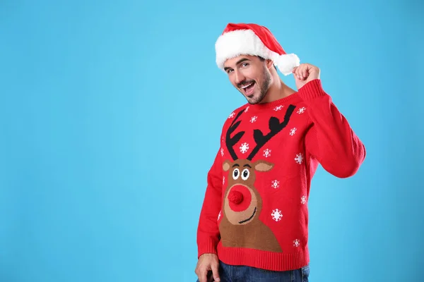 Portrait of young man in Christmas sweater and Santa hat on light blue background. Space for text — Stock Photo, Image