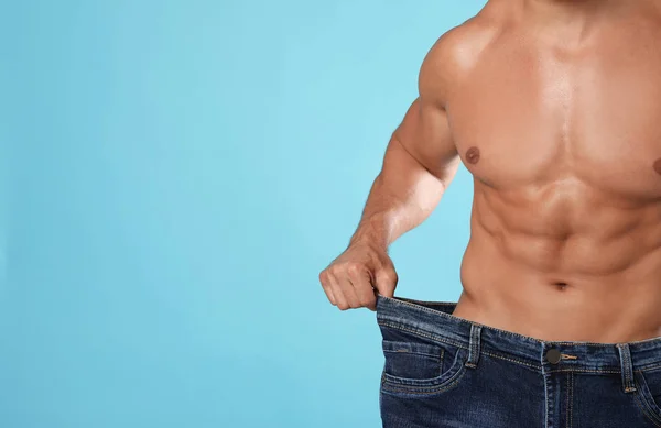 Jonge man met slank lichaam in oude big size jeans op licht blauwe achtergrond, close-up weergeven. Ruimte voor tekst — Stockfoto