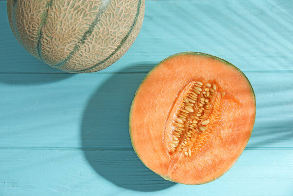 Tasty ripe cantaloupe melons and palm leaf shadow on light blue wooden table, flat lay