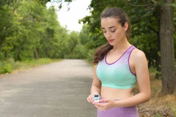 Mujer joven comprobando el pulso con dispositivo médico después de entrenar en el parque. Espacio para texto — Foto de Stock