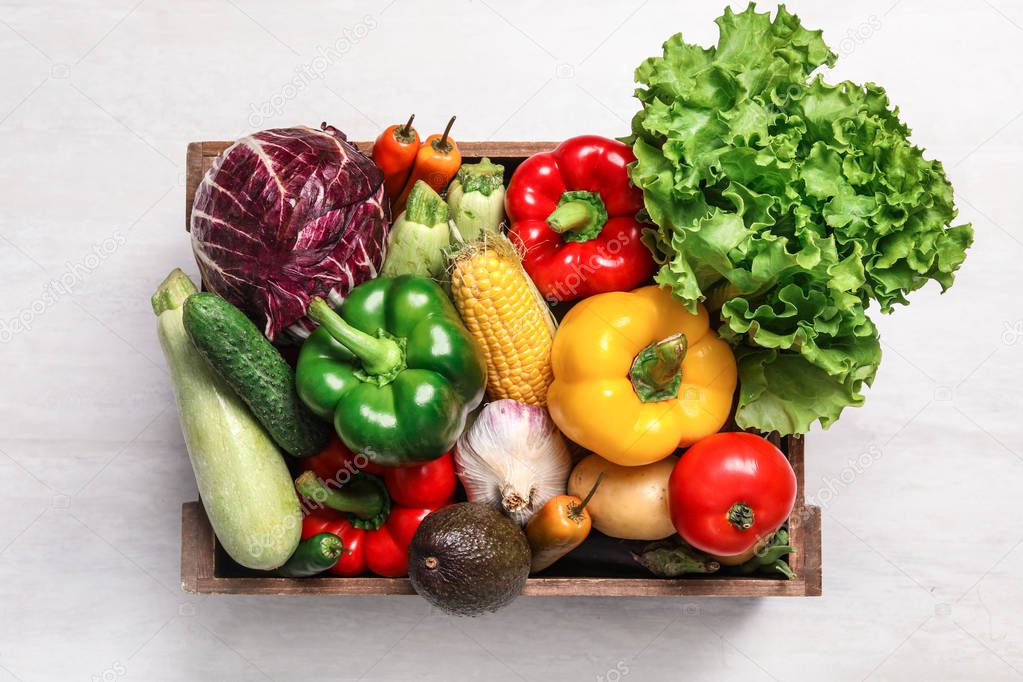 Crate with different fresh vegetables on light background, top view