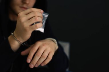 Elleri kelepçeli olarak gözaltına alınan adam, koyu arka plana karşı uyuşturucu içeren çantayı tutuyor, mesaj için yer var. Ceza hukuku