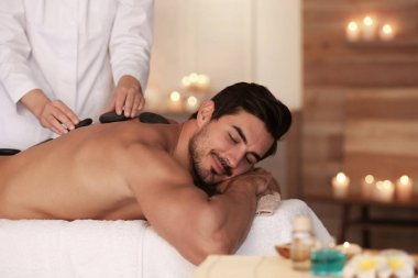 Yakışıklı genç adam spa salonunda sıcak taş masajı alan, metin için alan