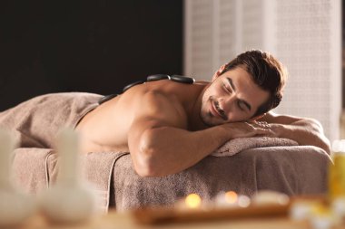 Spa salonunda sıcak taş masajı alan yakışıklı genç adam