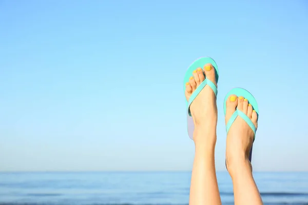 Close-up van de vrouw dragen flip flops in de buurt van zee, ruimte voor tekst. Strand accessoires — Stockfoto