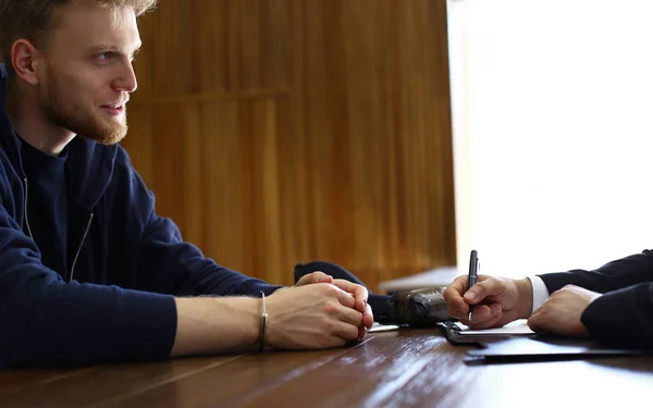 Police officer interrogating criminal in handcuffs at desk indoors — Stock Photo, Image