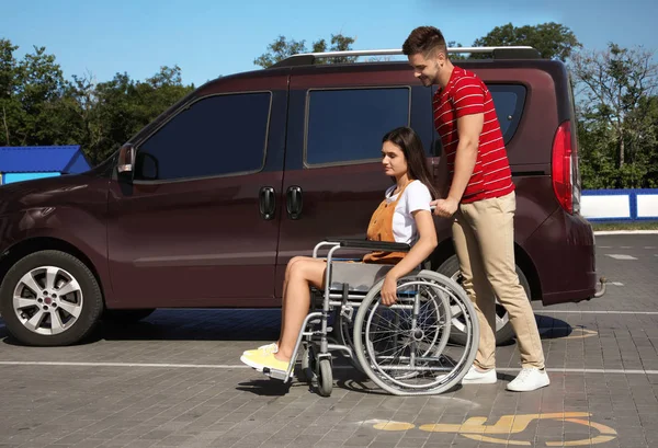 Młody mężczyzna z kobietą na wózku inwalidzkim w pobliżu van na parkingu — Zdjęcie stockowe